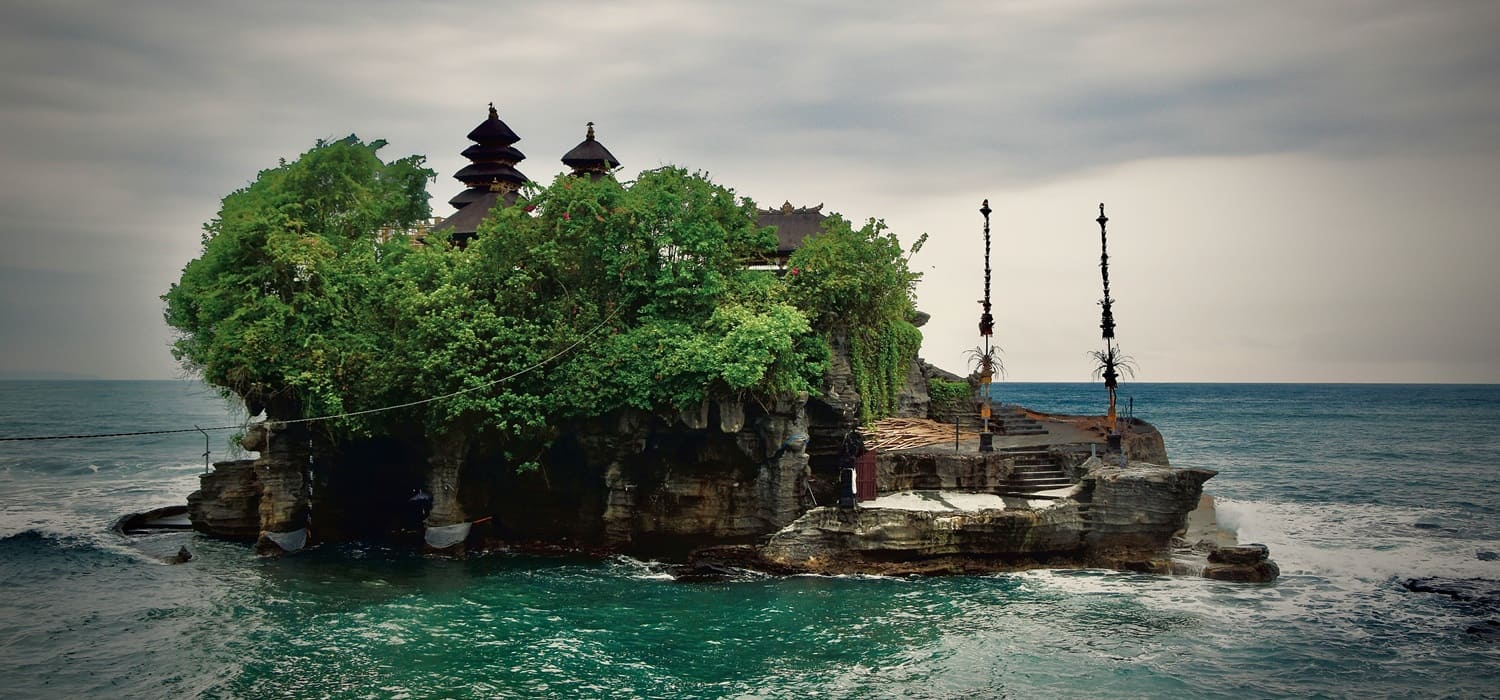 A rugged craggy stone pathway leading traveling visitors toward the sacred sea shrine of Tanah Lot during low tide